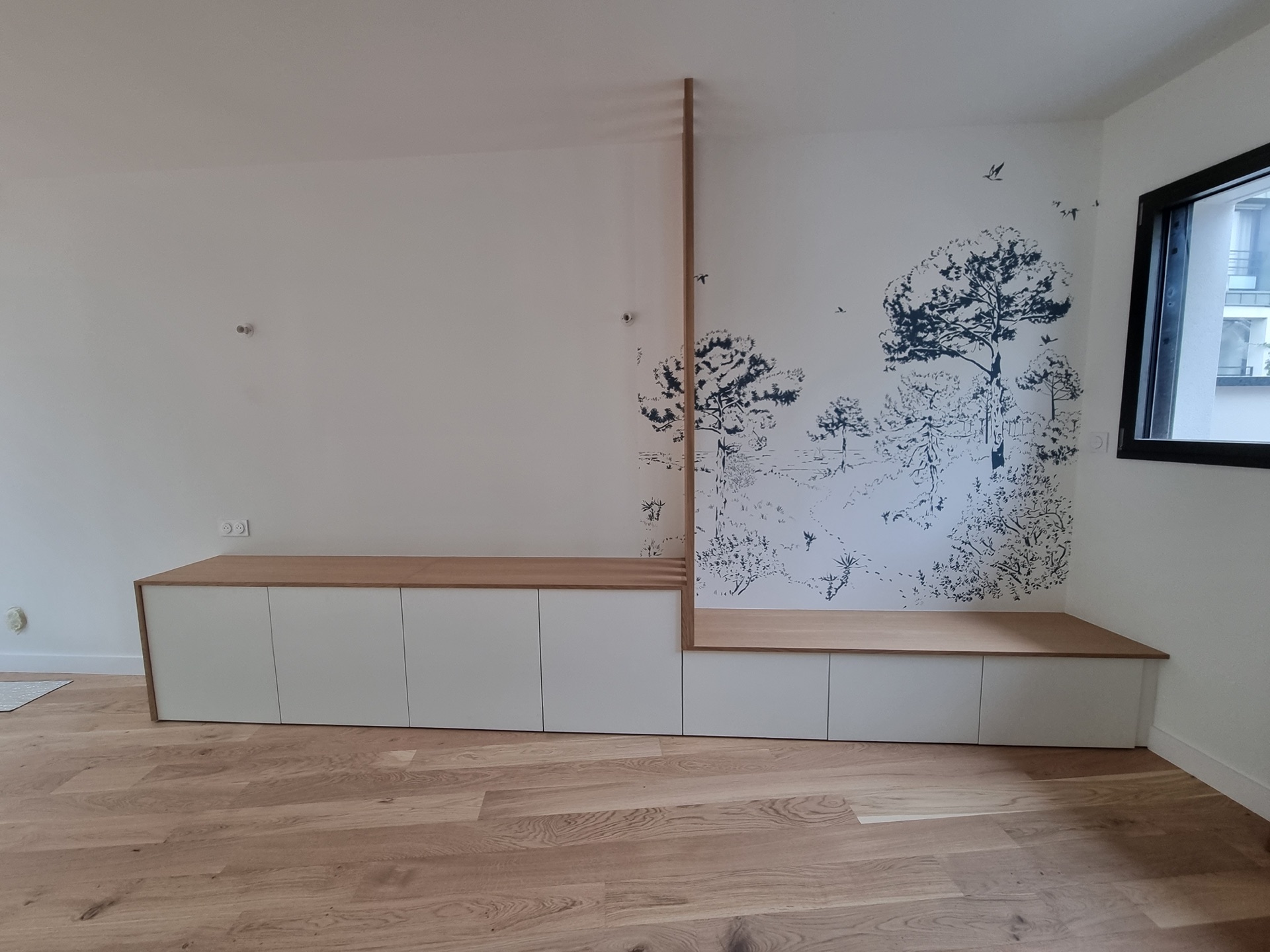 Banc-rangement intégré chêne et meuble bas sur-mesure devant fresque paysage panoramique dans le salon à Biarritz